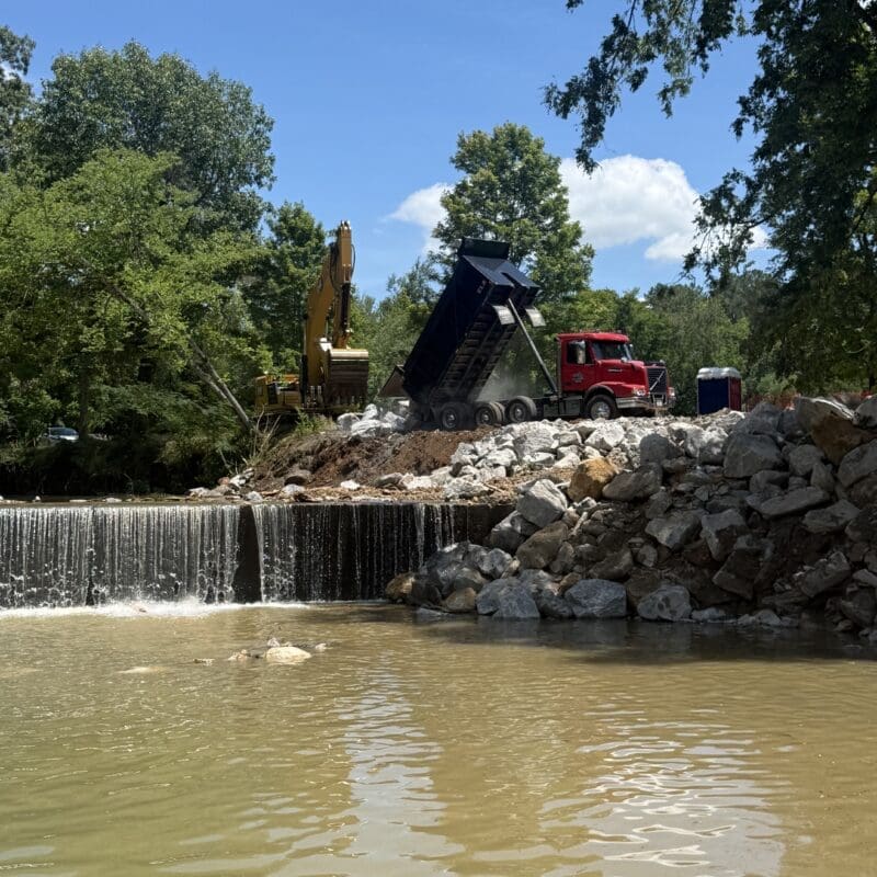 JD Lee Excavating crew placing riprap with an excavator and dump truck for creek bank erosion control in Middle Tennessee.