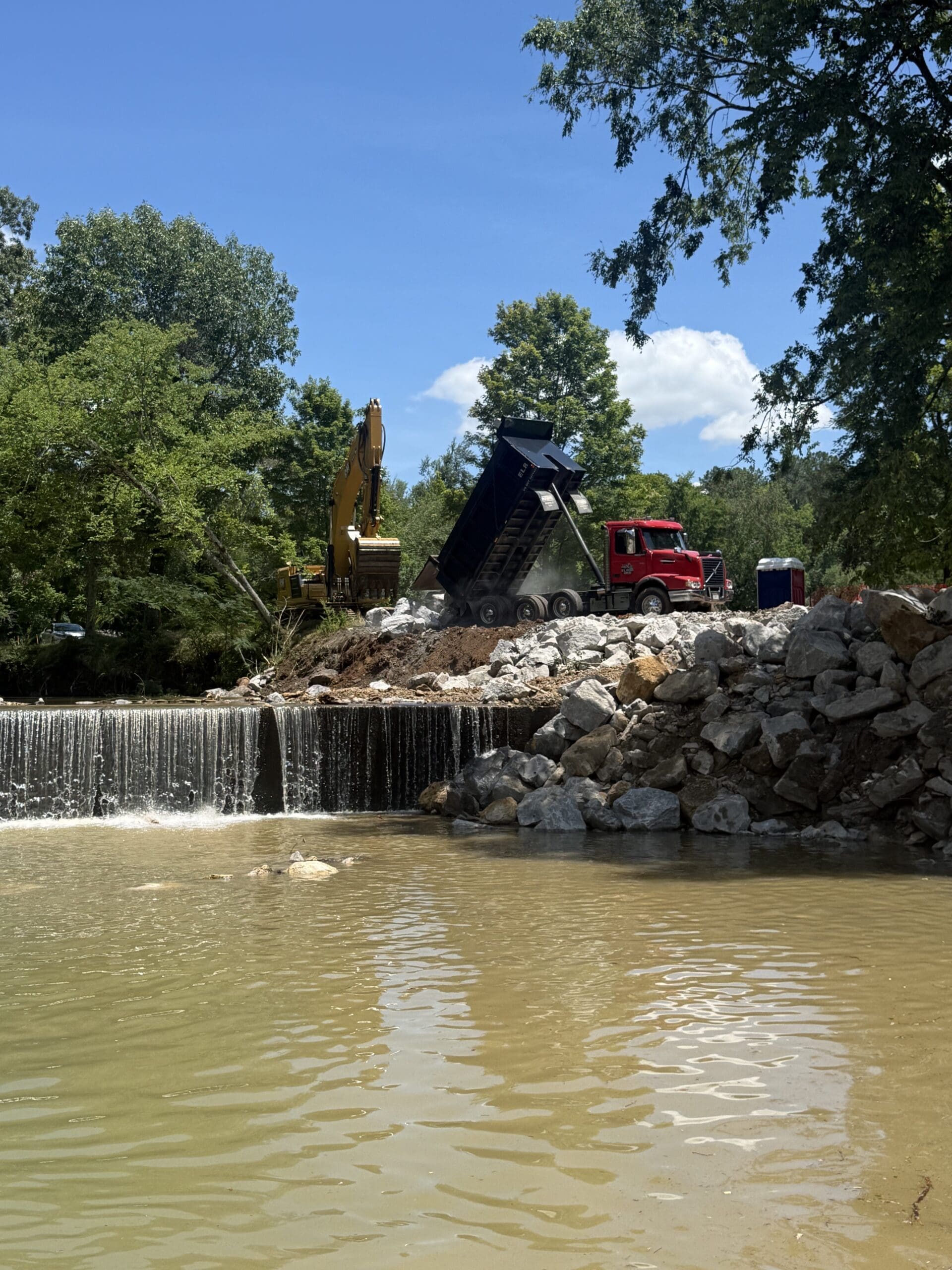 JD Lee Excavating crew placing riprap with an excavator and dump truck for creek bank erosion control in Middle Tennessee.